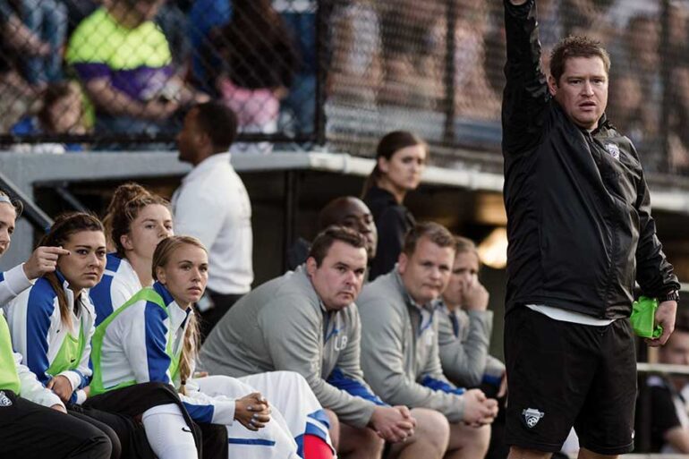 Matt Beard, head coach of the Boston Breakers, in fron of the team bench. by Mike Gridley